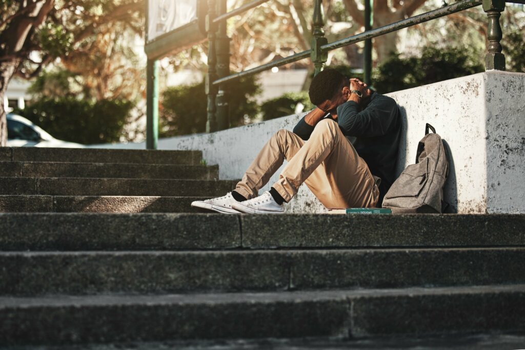 Sad, depression and black man with anxiety at college, stress and headache from education on the stairs at campus. Depressed, frustrated and student with a mental health problem crying at university.